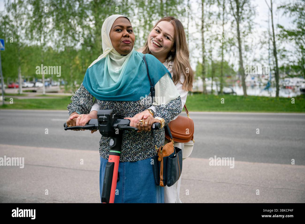 Zwei ethnisch unterschiedliche Frauen, die zusammen Elektroroller fahren Stockfoto