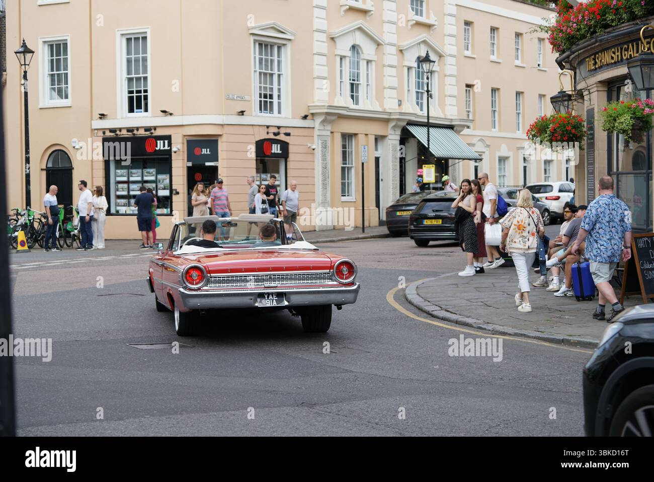 Klassisches rotes Cabriolet, das durch eine geschäftige Kreuzung fährt. Greenwich, London, England Stockfoto