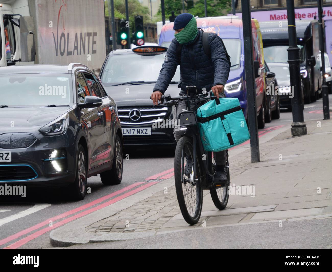 Ein maskierter Deliveroo-Radfahrer fährt auf dem Bürgersteig in Central London, Großbritannien, und äußert anhaltende Bedenken hinsichtlich der Straßensicherheit, des Zugangs zu Fußgängern und der städtischen Lieferpraktiken Stockfoto
