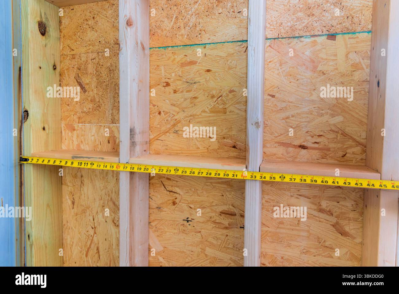 Holzbalkenrahmen werden mit Bandmaß bei Hausverbesserungsarbeiten in neu errichtetem Raum gemessen. Stockfoto