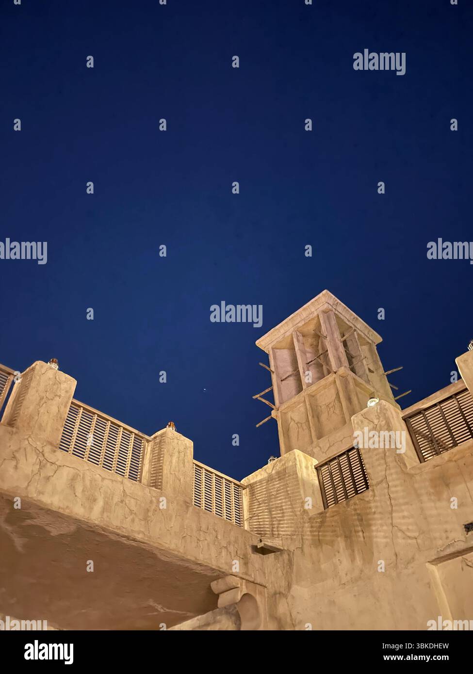 Das traditionelle Dach des Al-Seef strahlt bei Nacht in einem leuchtenden Licht und die Silhouette des Windturms vor einem tiefblauen Himmel. - Smartphone-aufgenommenes Stockfoto