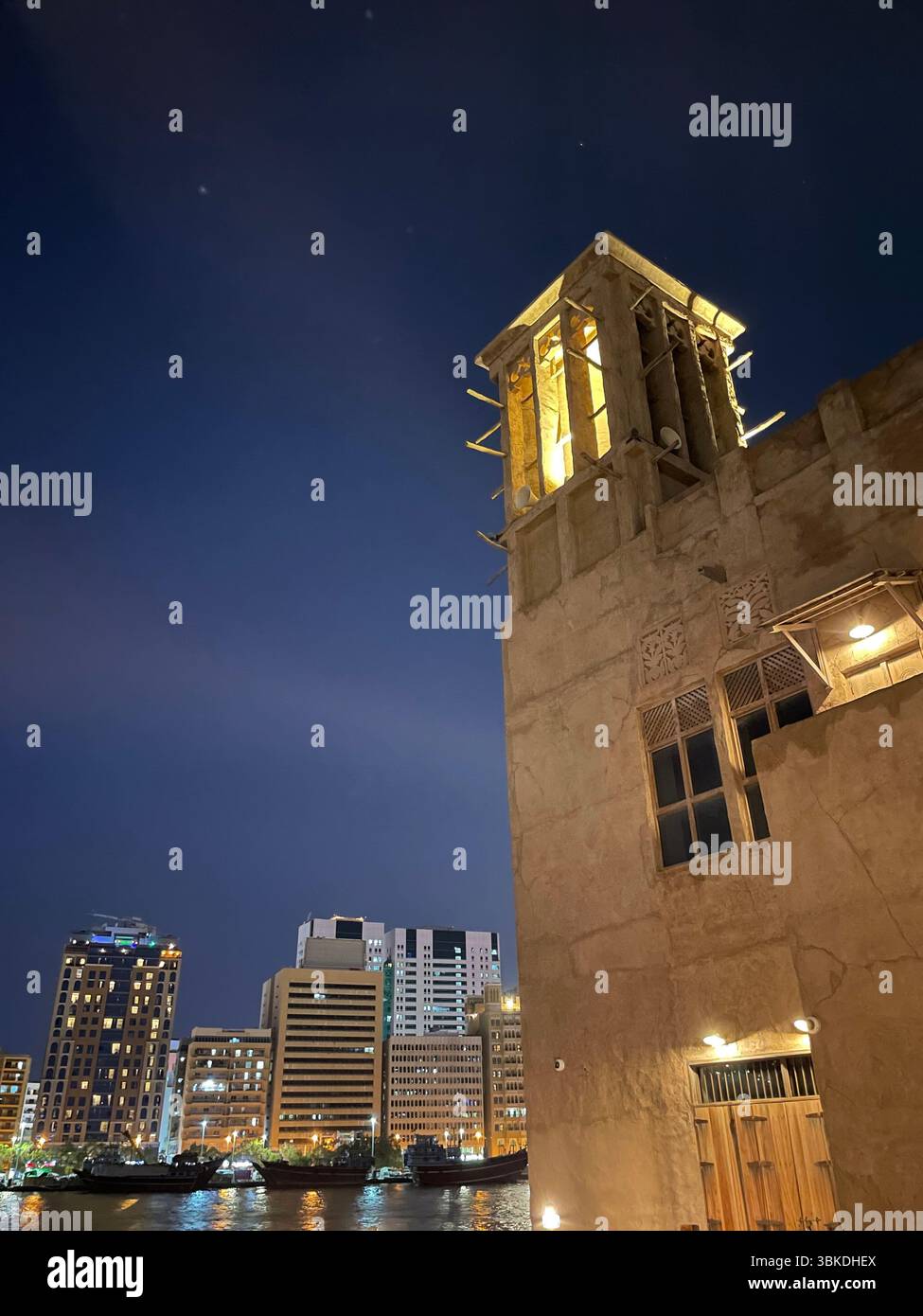 Nachtansicht auf die traditionellen Emirati-Häuser von Al Seef auf der rechten Seite und die modernen Bur Dubai-Gebäude auf der linken Seite entlang des malerischen Dubai Creek. Stockfoto