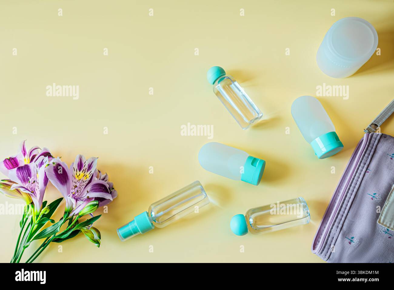 Flache Komposition von Reisetoilettenflaschen, Kosmetikbeutel und frischen Blumen auf pastellfarbenem Hintergrund. Helle, saubere und feminine Reiseutensilien Stockfoto