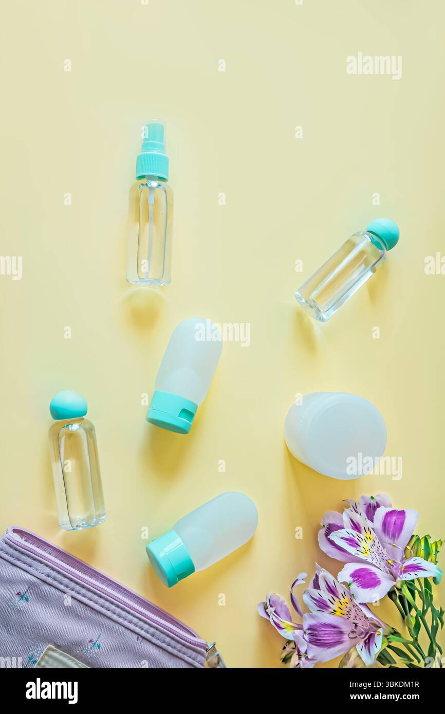 Anordnung von Hygienebehältern und einem kleinen Blumenbeutel mit violetter Alstroemeria auf weichgelbem Hintergrund. Saubere, organisierte und elegante Reisen Stockfoto