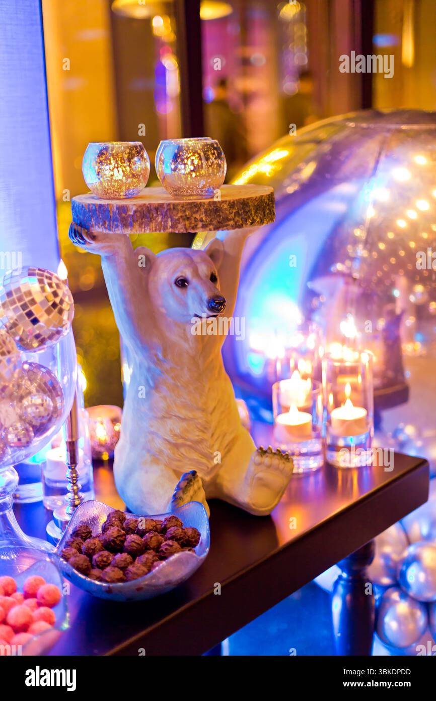 Eine bezaubernde Eisbärenskulptur mit einer Holzplatte mit zwei glitzernden Kerzenleuchtern, die festlich eingerichtet ist, darunter Discokugeln und Süßigkeiten. Stockfoto