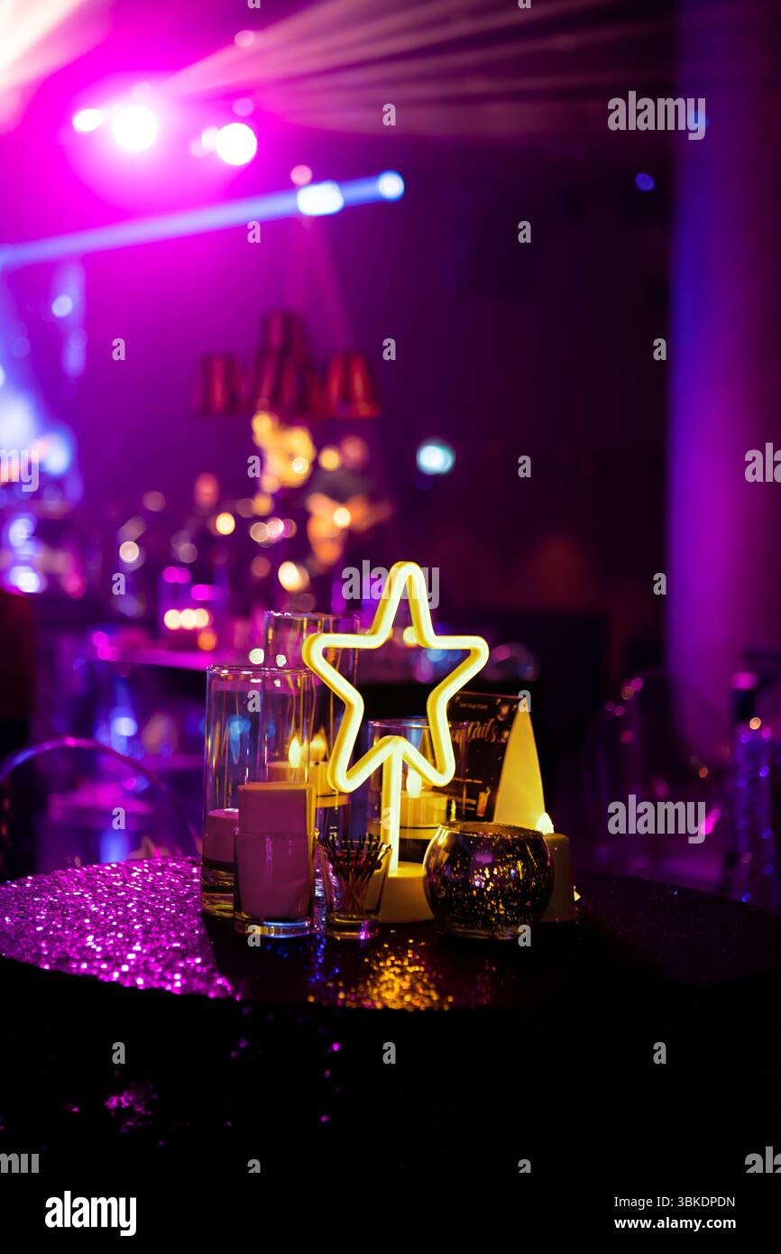 Ein Tischaufsatz mit einem leuchtenden Neonstern, Kerzen und einer Pailletten-Tischdecke, in hellem lila Licht getaucht. Stockfoto