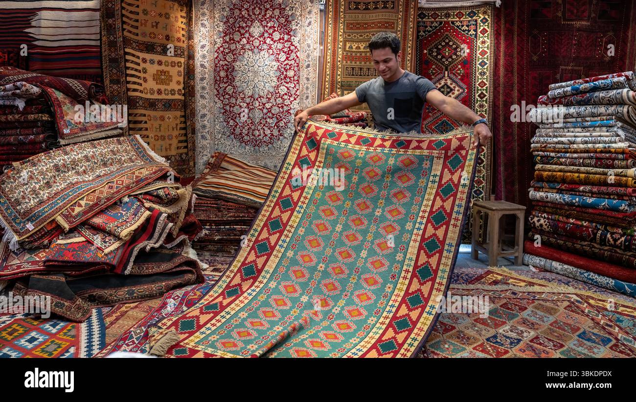 Isfahan, Iran - 30. April 2019: Mann mit einem reich gemusterten traditionellen persischen Teppich, der lebendige Textilien und Handwerkskunst zeigt Stockfoto