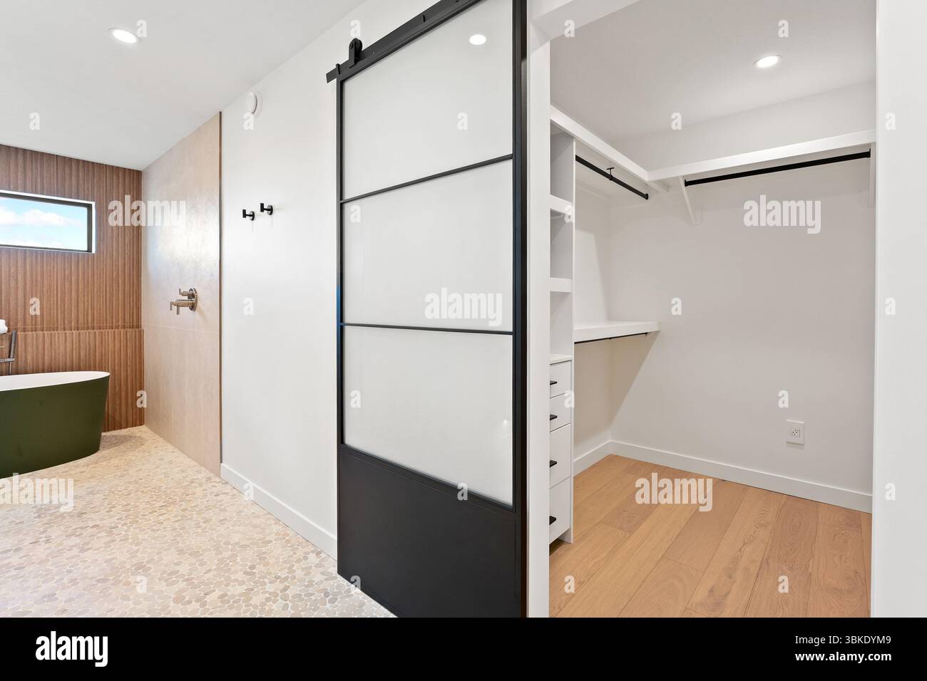 Großer begehbarer Kleiderschrank mit schwarzer Tür und weißer Verkleidung. Der Schrank ist sehr sauber und organisiert Stockfoto