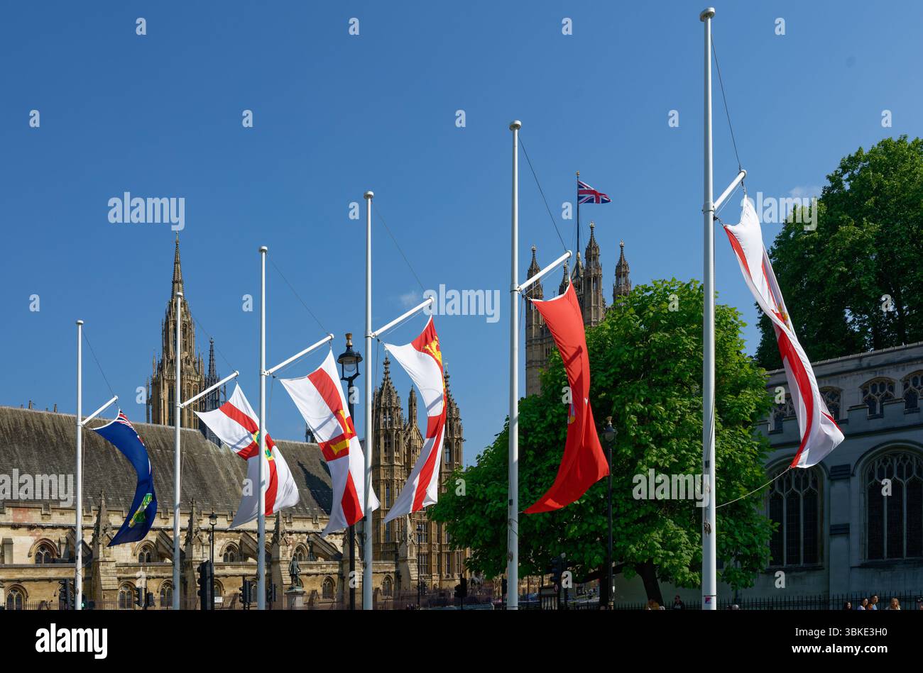 Fahnen fliegen mit den Houses of Parliament dahinter, blauer Himmel, sonniger Tag in London, England Stockfoto
