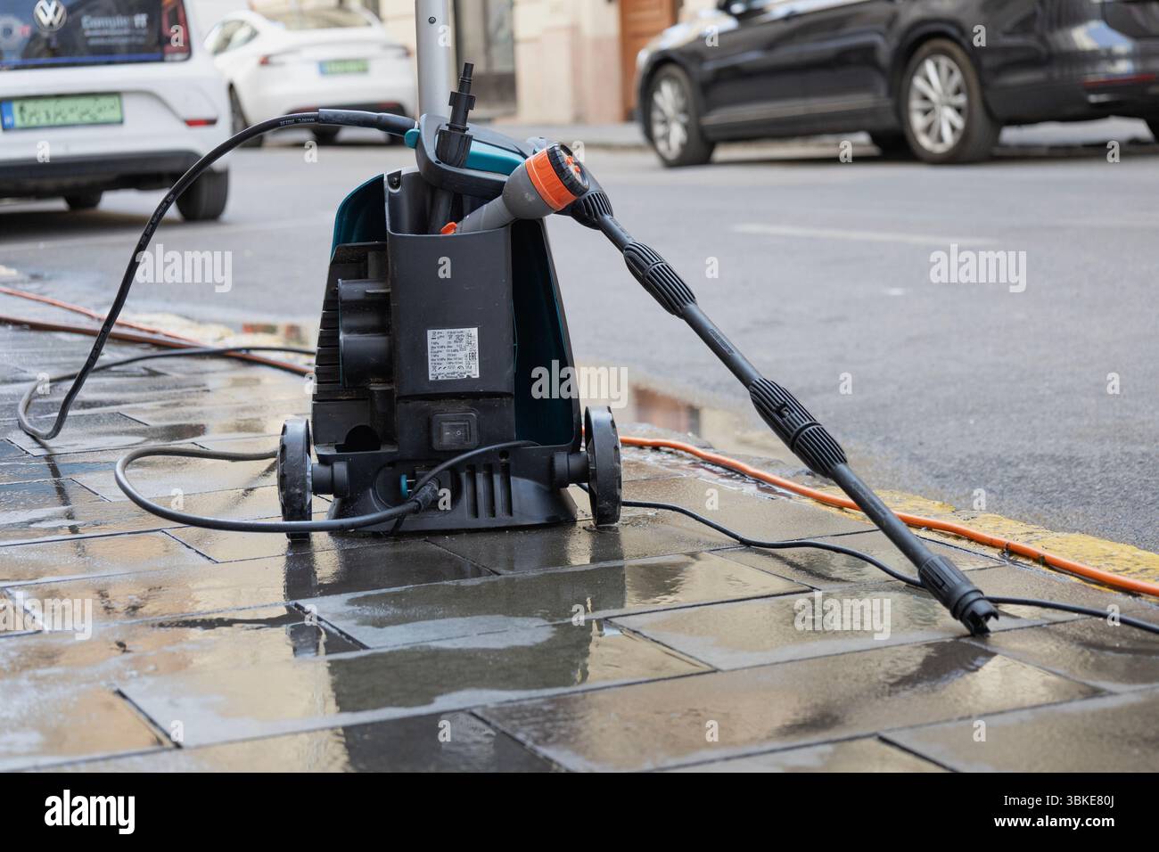 Morgenatmosphäre, wenige Leute auf den Straßen, die das nutzen, um die Gehwege zu reinigen. Nahaufnahme eines Hochdruckreinigers auf dem nassen Bürgersteig Stockfoto