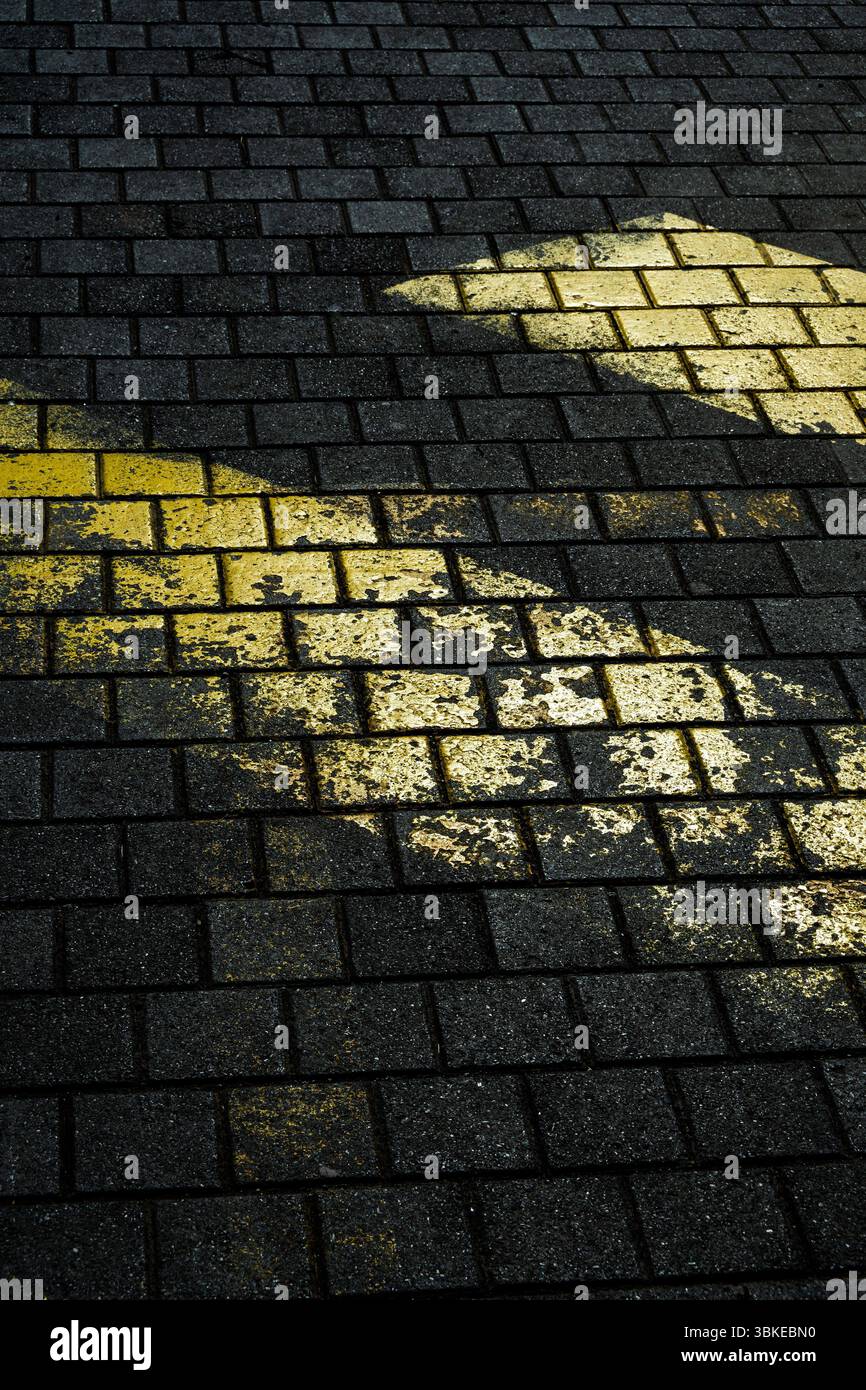 Verblasste gelbe Markierungen auf dunklem, strukturiertem Straßenpflaster aus Stein schaffen einen auffälligen Kontrast. Stockfoto