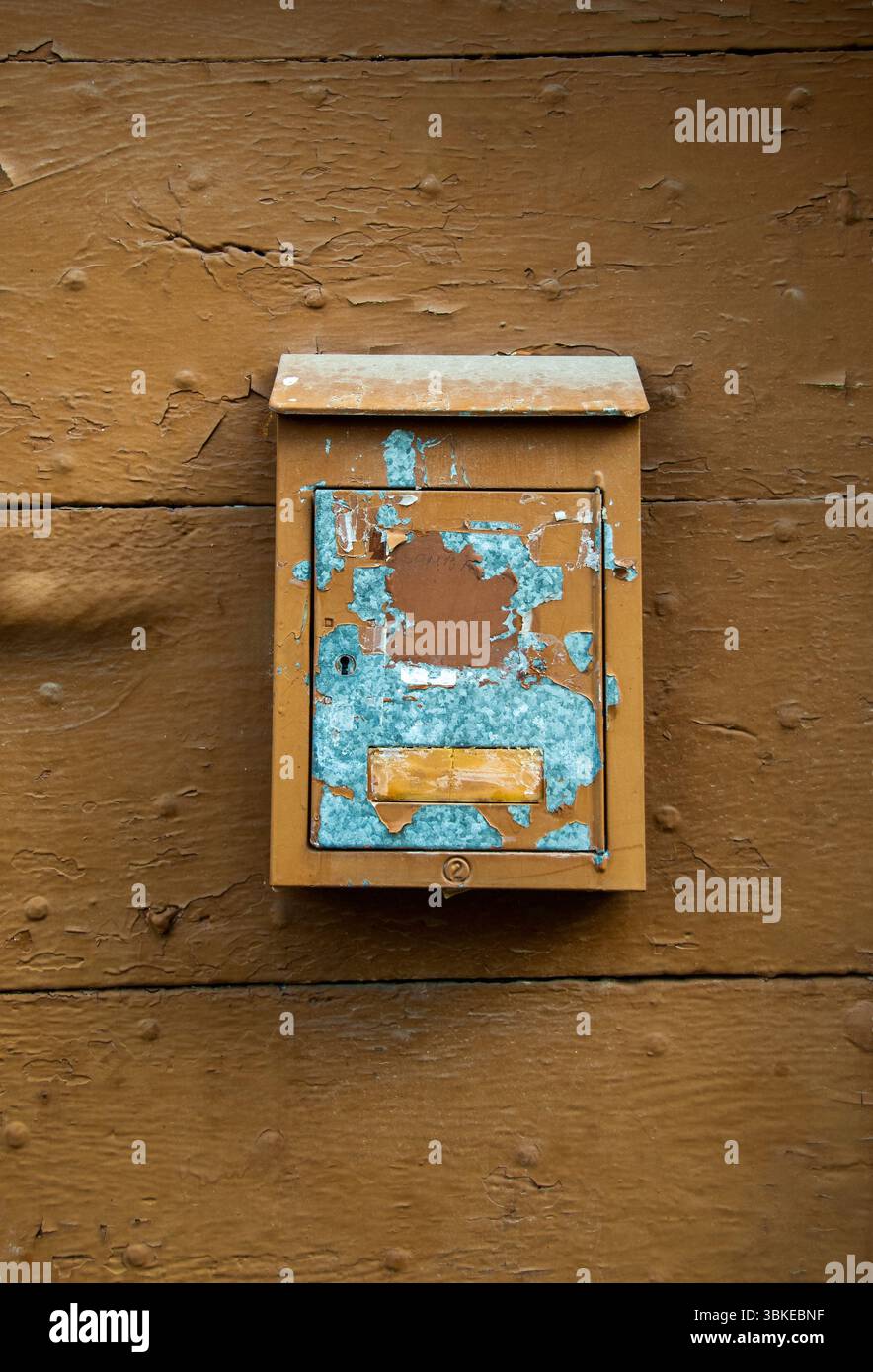 Ein verwitterter Briefkasten hängt an einer rustikalen Holzwand mit abgebrochener Farbe in Blau- und Brauntönen. Auvergne. Frankreich Stockfoto