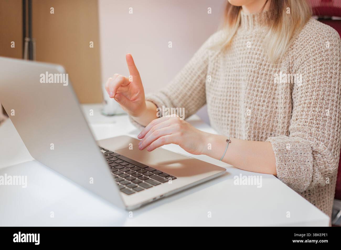 Frau macht bei Online-Videoanrufen von zu Hause aus mit einem modernen Laptop auf den Punkt. Gelegenheitsarbeiterin hebt den Zeigefinger, während sie etwas erklärt Stockfoto
