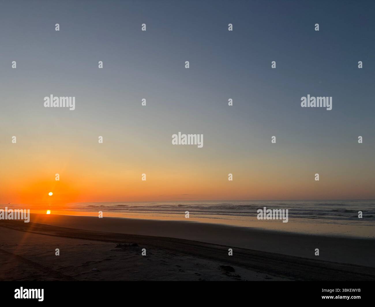 Goldene Sonne taucht einen ruhigen Strand und ruhige Meereswellen in einen wunderschönen Sonnenaufgang. Eine ruhige, friedliche Küstenlandschaft - Smartphone-aufgenommenes Stockfoto