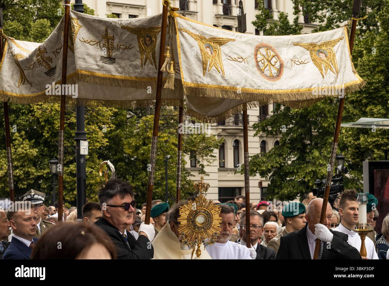Priester, Altardiener und Gläubige Laien nehmen an einer Fronleichnamsprozession unter einem verzierten Baldachin Teil, die eine vergoldete Monstranz trägt Stockfoto