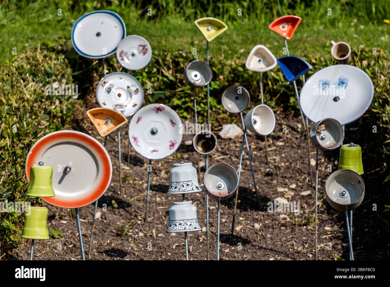 Teller, Tassen und Schüsseln sind auf Metallstangen in einem Blumenbeet in der Rue de la Corderie in Port-d'Envaux, Nouvelle-Aquitaine, Frankreich, montiert. Sie umfassen einen Teller mit rotem Rand, blumige Teller, umgedrehte Tassen, grüne Becher und kleine dreieckige Schüsseln. Das Motiv passt zum deutschen Sprichwort "Über den Tellerrand schauen". Es bezieht sich auf eine offene, neugierige Haltung, bei der man bereit ist, die eigenen Grenzen zu überschreiten und neue Dinge zu lernen. Der Ausdruck wird oft im Zusammenhang mit Kosmopolitismus, einem Perspektivenwechsel oder Innovation verwendet. Denken über den Tellerrand hinaus. Die Deko Stockfoto