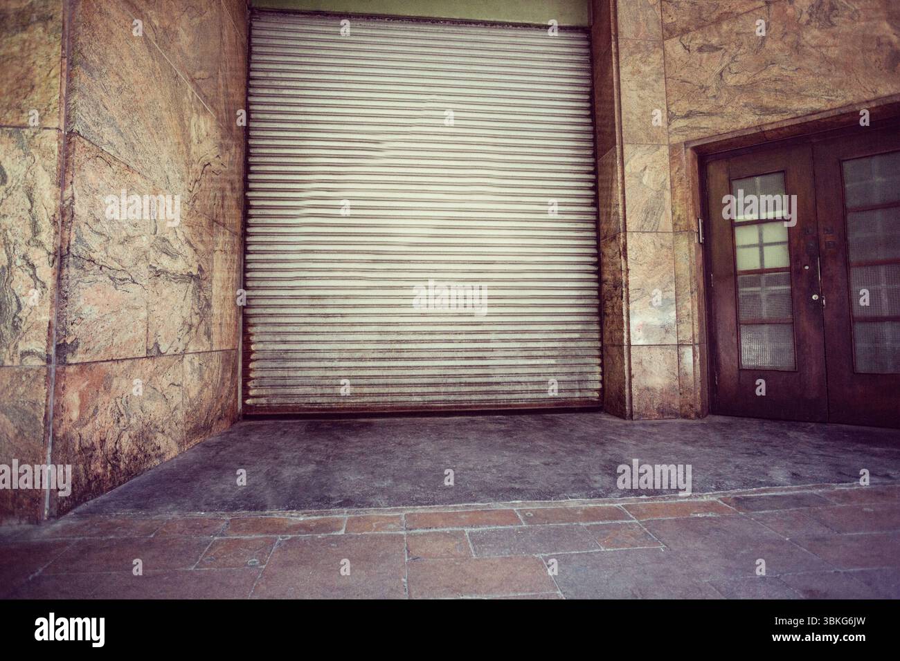 Der Eingang zeigt einen eingelassenen Eingang in flachem Design mit Marmorwänden, Metallladen und Holztüren Stockfoto