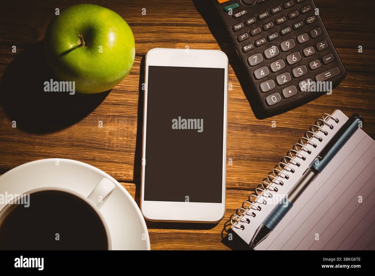 Ein Flachtisch über dem Kopf zeigt ein weißes Smartphone mit grünem Apfel, Kaffee, Rechner, Notebook und Stift Stockfoto