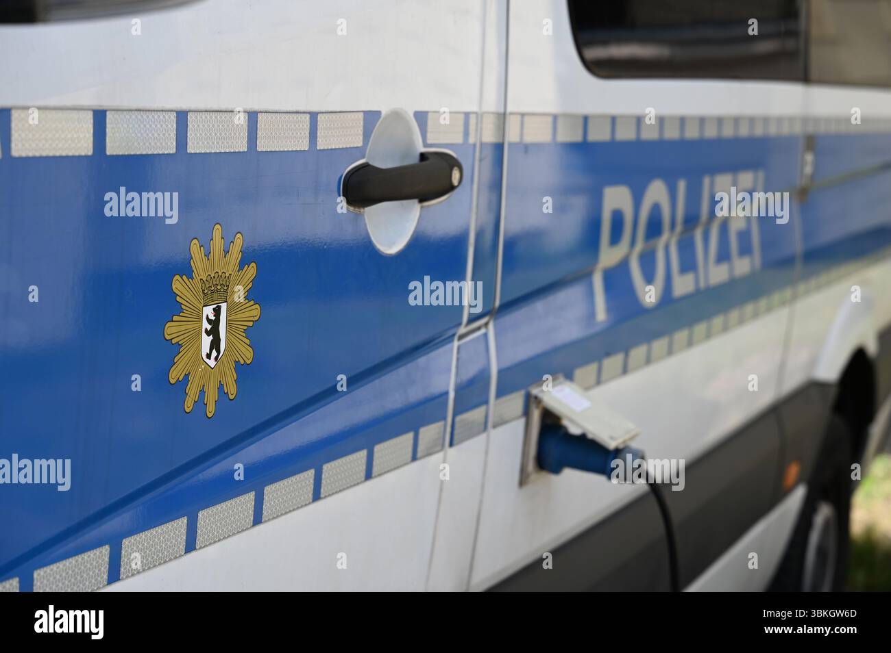 Berlin, Deutschland. Juni 2025. Ein Bus der Berliner Polizei steht auf dem Parkplatz und ist mit einem Stromkabel verbunden. Das Polizeilogo und ähnliche Schriftzeichen sind an der Tür zu sehen. Quelle: Michael Brandt/dpa/Alamy Live News Stockfoto