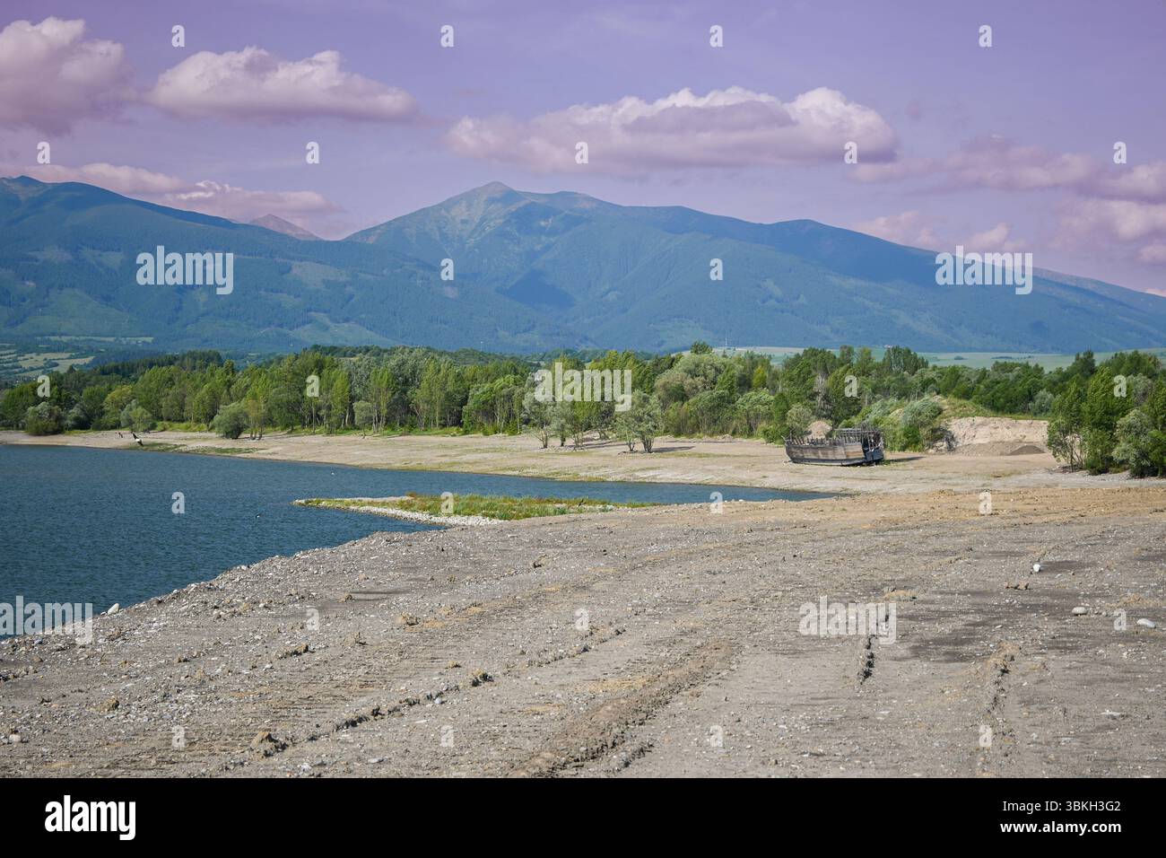 Das abfallende Wasser zeigt ein verlassenes Schiff auf einem trockenen Seebett mit Bergen und wolkigem Himmel im Hintergrund. Stockfoto