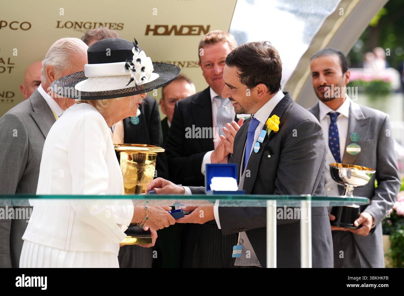 Königin Camilla begrüßt Trainer Jerome Reyneir nach dem Sieg in den Jubilee Stakes von Queen Elizabeth II., als König Karl III. (Links) während des fünften Tages von Royal Ascot auf der Ascot Racecourse in Berkshire zusieht. Bilddatum: Samstag, 21. Juni 2025. Stockfoto