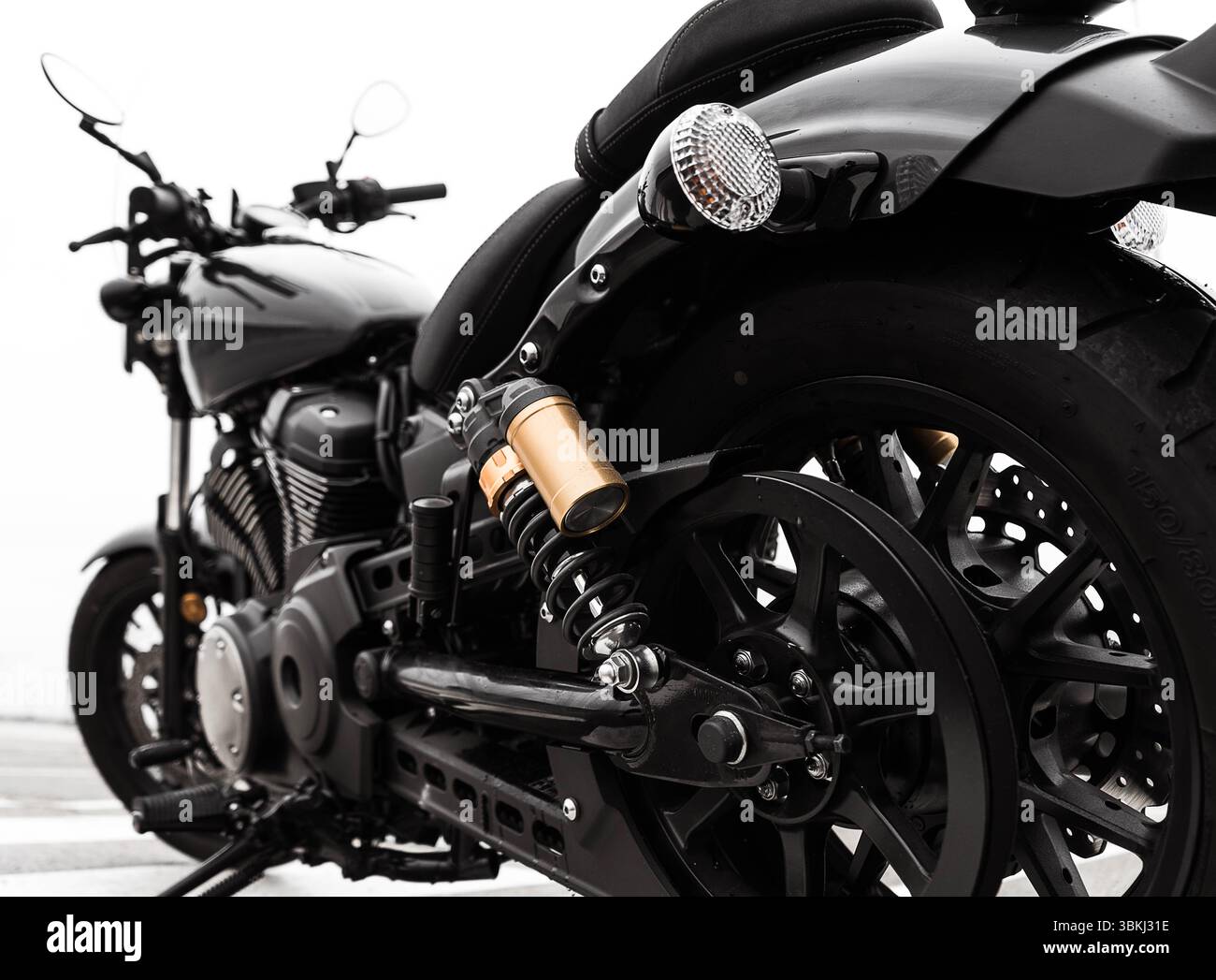 Die Abbildung zeigt eine Nahansicht eines schwarzen Motorrads mit Hinterrad, Federung und Rücklicht. Das Design des Motorrads ist schwarz Stockfoto