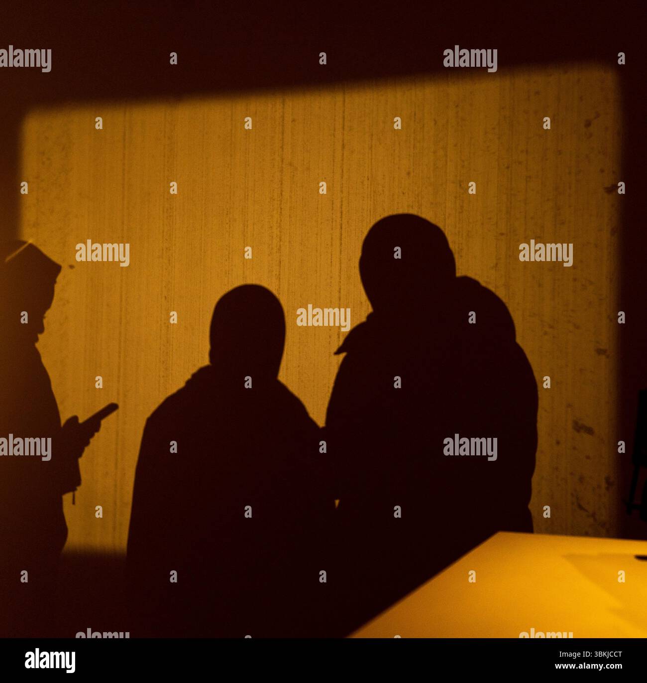 Drei Personen stehen in einem schwach beleuchteten Raum mit gelbem Licht hinter der Wand. Das Bild ist eine Silhouette der Individuen, Creat Stockfoto