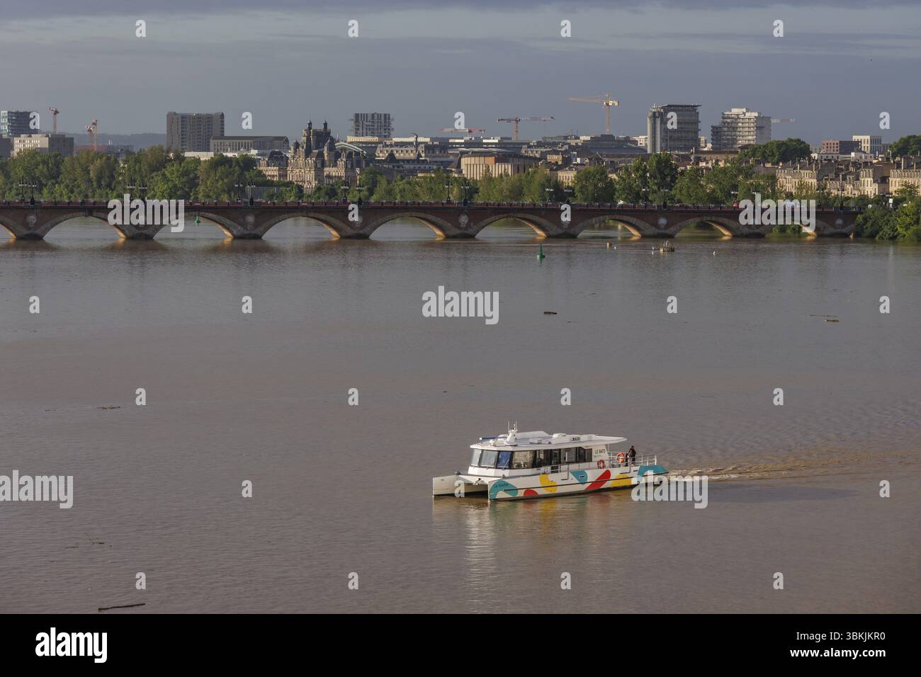 Blick auf den städtischen Fluss mit einer Brücke und einem farbenfrohen Boot im Vordergrund, Bordeaux, garonne, frankreich Stockfoto