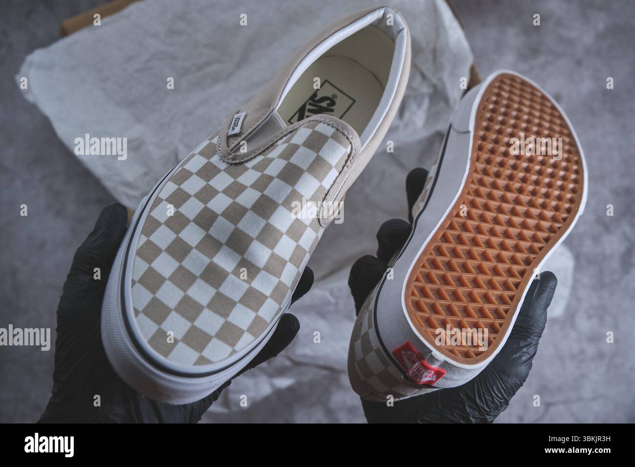 Mit Handschuhen öffnen Sie einen Schuhkarton für Vans, der neue karierte Slip-on-Schuhe vor einem prägnanten Hintergrund enthüllt Stockfoto