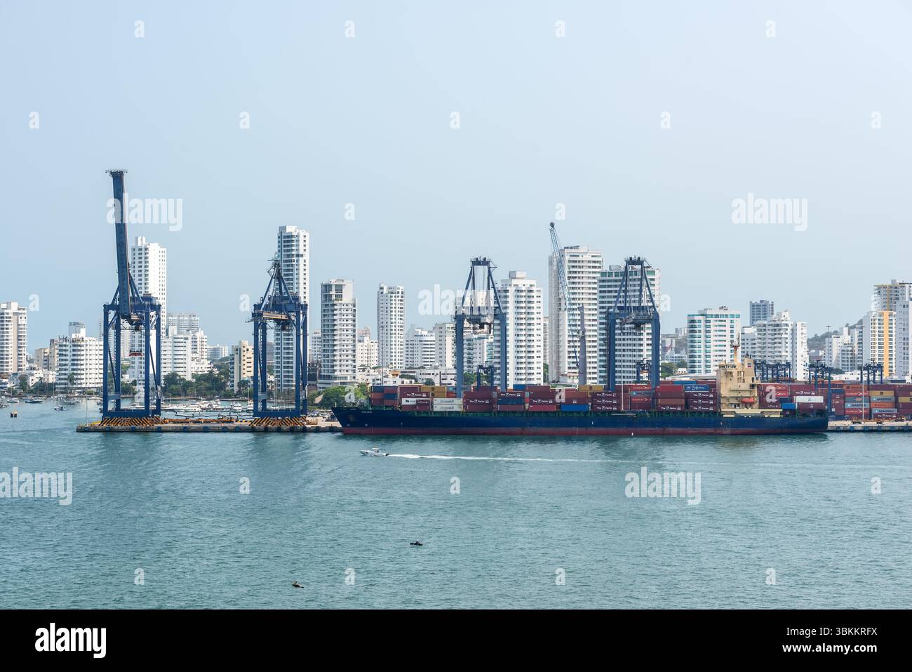 Cartagena, Kolumbien - 12. April 2024: Die Hafenszene zeigt das Containerschiff Chloe D, Kräne und Schiffscontainer mit den hohen Gebäuden von Cartagena Stockfoto