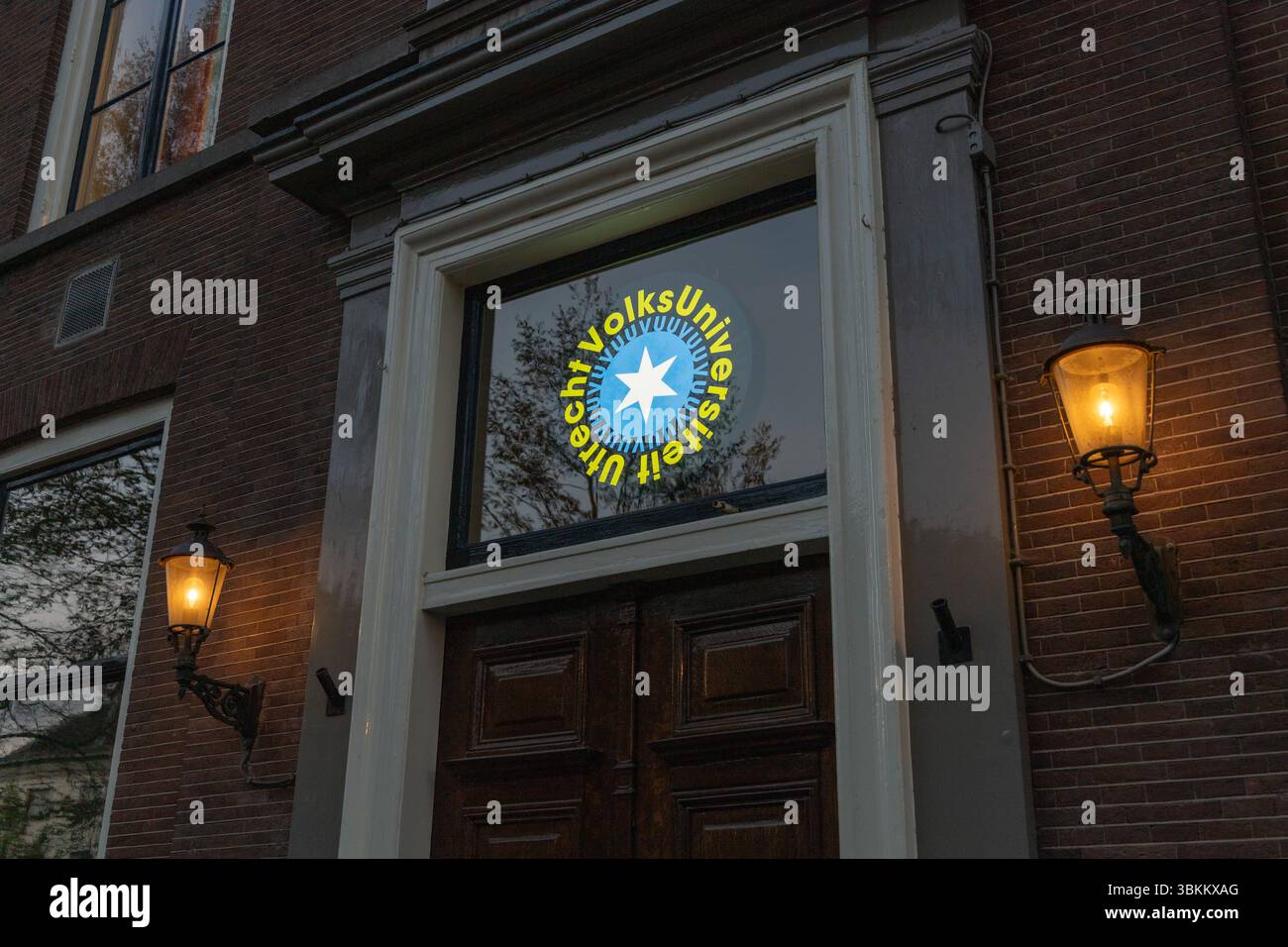 Logo der Volksuniversiteit Utrecht auf einem Fenster mit Sterndesign und Text in kreisförmigem Layout, reflektiert mit Bäumen im Hintergrund. Utrecht, N Stockfoto