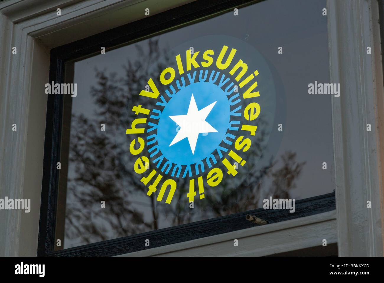 Logo der Volksuniversiteit Utrecht auf einem Fenster mit Sterndesign und Text in kreisförmigem Layout, reflektiert mit Bäumen im Hintergrund. Utrecht, N Stockfoto