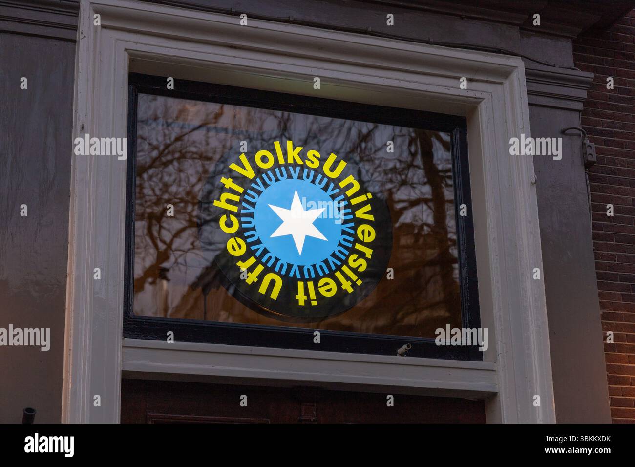 Logo der Volksuniversiteit Utrecht auf einem Fenster mit Sterndesign und Text in kreisförmigem Layout, reflektiert mit Bäumen im Hintergrund. Utrecht, N Stockfoto