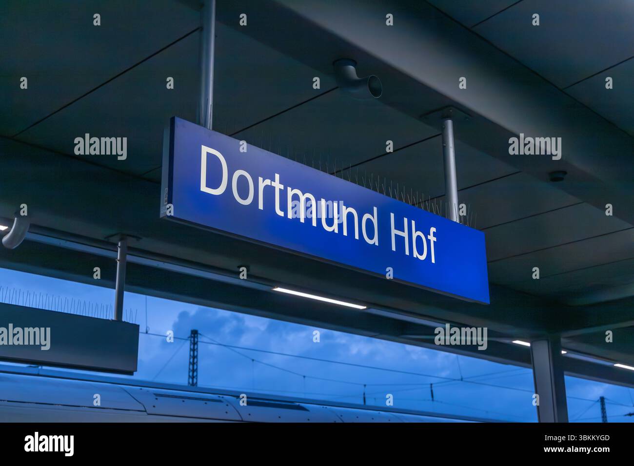 Blaues Schild mit der Aufschrift 'Dortmund Hbf' (Hauptbahnhof) hängt über einem Bahnsteig. Öffentliche Verkehrsmittel. Dortmund, Deutschland. 30. März 2025. Stockfoto