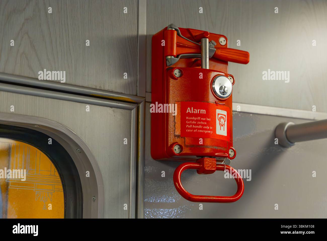 Nahaufnahme eines roten Notalarmgriffs in einem Zug, montiert an einer Metallwand, mit zweisprachigen Sicherheitsanweisungen in Deutsch und Englisch. Stockfoto