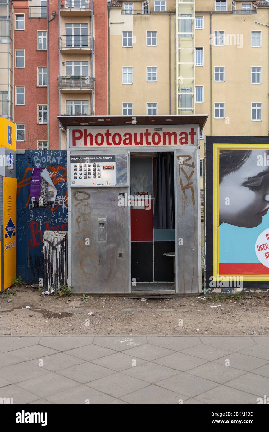 Fotoautomat im Vintage-Stil auf einer mit Graffiti bedeckten Straße in Berlin, Deutschland, mit städtischen Gebäuden und Plakaten im Hintergrund. Berlin, Deutsch Stockfoto