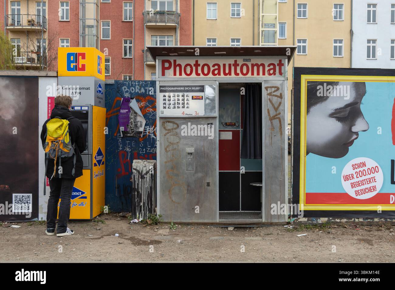 Fotoautomat im Vintage-Stil auf einer mit Graffiti bedeckten Straße in Berlin, Deutschland, mit städtischen Gebäuden und Plakaten im Hintergrund. Berlin, Deutsch Stockfoto