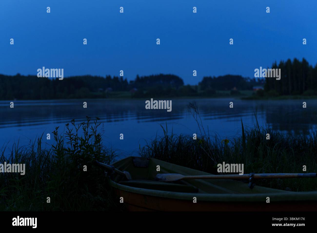 Ein ruhiger See in der Mittsommernacht mit einem Ruderboot an der Küste. Stockfoto