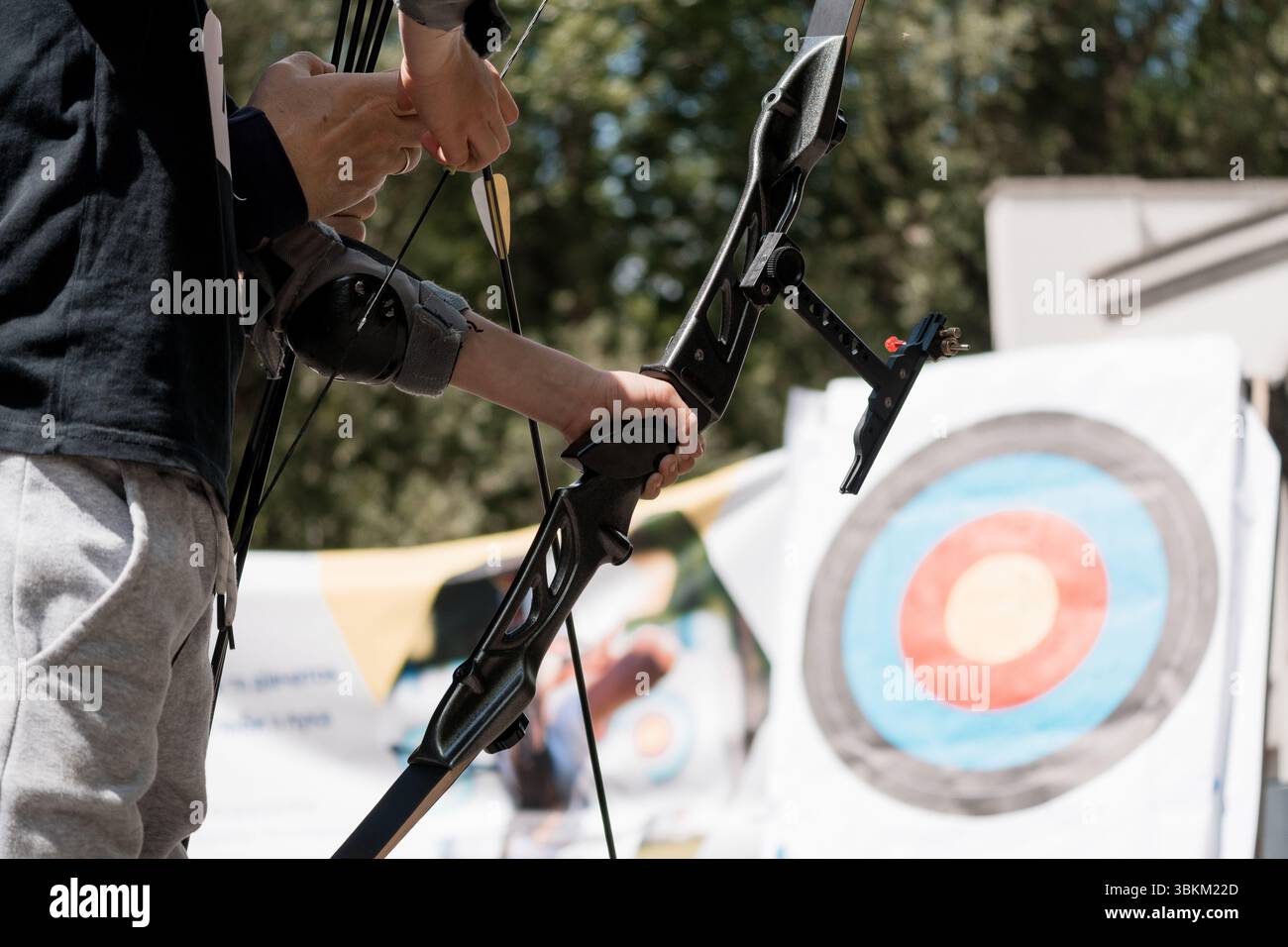 Ein junger Bogenschütze konzentriert sich auf das Zielen und Schießen mit einem modernen Verbundbogen auf einen Outdoor-Zielbereich, der die Sporttechnik, den Jugendsport, demonstriert Stockfoto