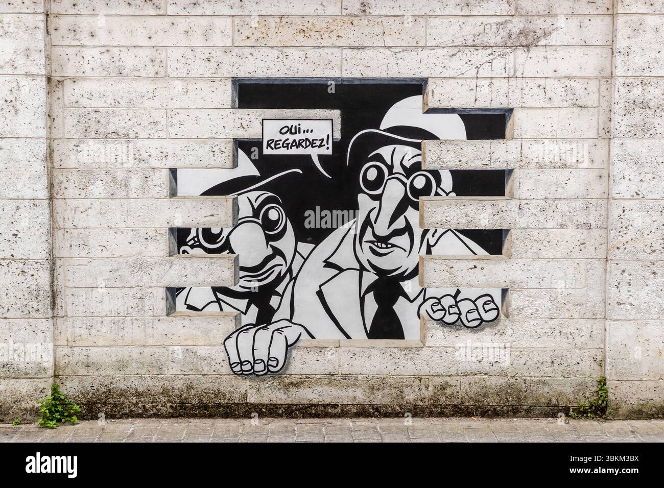 Das Wandgemälde aus der Serie "Réalité, Sortie de Secours" (Realität, Notausgang), entworfen von Marc-Antoine Mathieu, zeigt Comicfiguren mit Sprechblasen, die aus der Wand zu platzen scheinen, Rue de Beaulieu, Angoulême, Nouvelle-Aquitaine, Frankreich. In dieser Szene schauen zwei Männer mit Hüten und runden Brillen durch eine größere Lücke, ihre Hände greifen den Rand der gemalten Steine. Die Sprechblase lautet "Oui... regardez!" Auf Englisch: 'Yes... look!' In sechs Panels erzählt die Serie eine komplette Geschichte: "Sehen Sie etwas? Ja, schauen Sie. Es ist genau das, was ich befürchtet habe. Was, noch eine Unterwelt Stockfoto