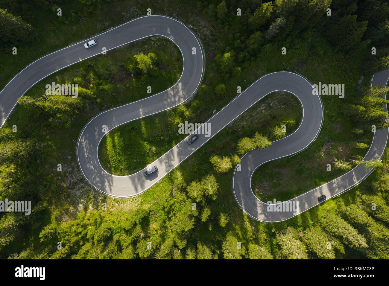 Kurvenreiche Straße führt durch üppiges Grün mit Autos entlang der malerischen Route in einer bergigen Gegend unter klarem blauem Himmel. Stockfoto