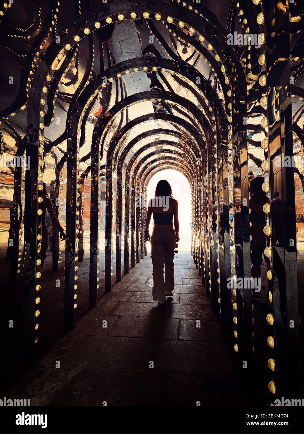 Frau, die den beleuchteten und spiegelnden Tunnel im Londoner Theaterviertel hinuntergeht. Die neue Infinity Chamber von Covent Garden befindet sich in Conduit Court Stockfoto