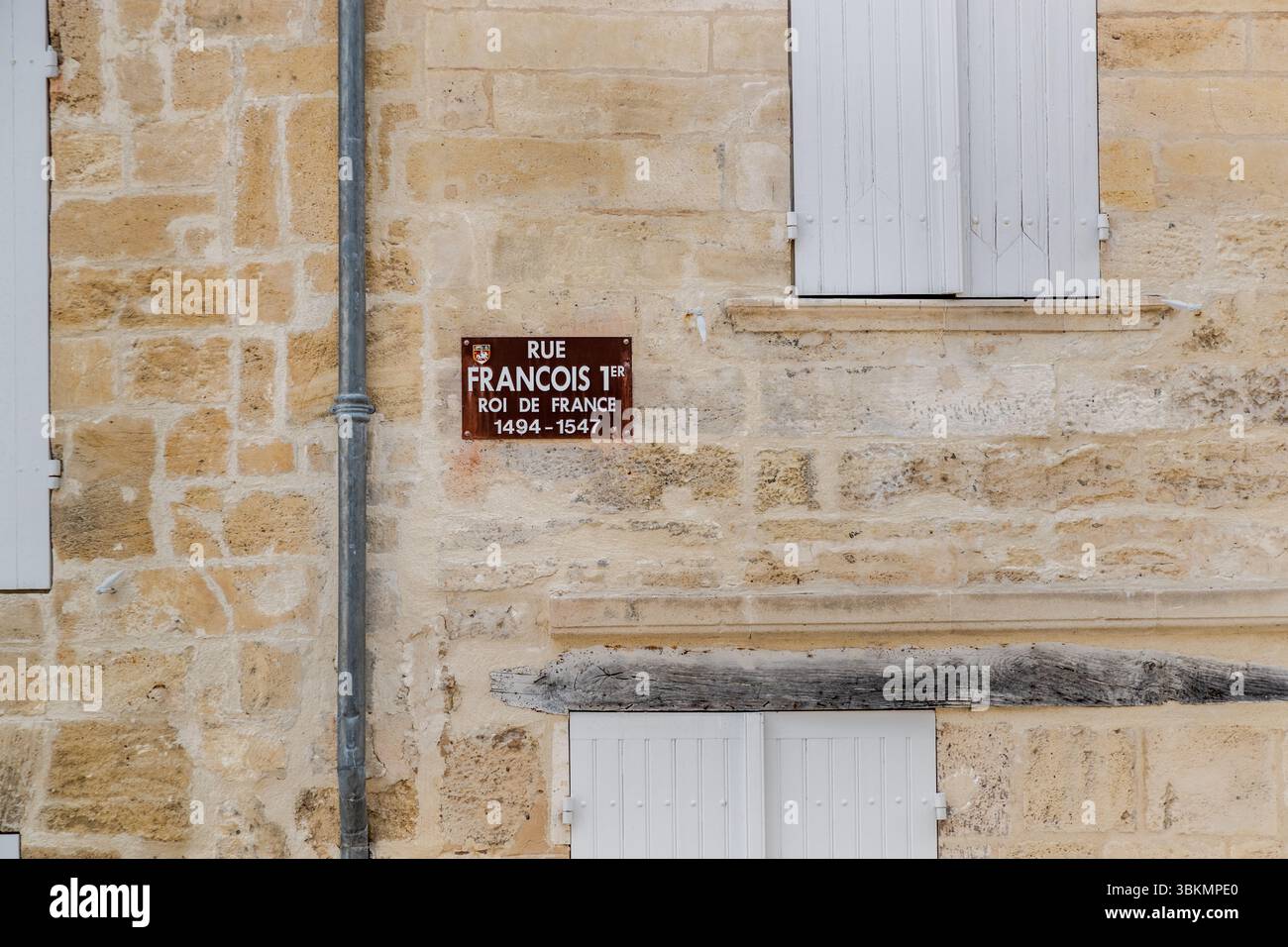 Straßenschild mit dem Namen: Rue Francois 1er, König von Frankreich und geboren in Cognac. Straßenschild in der Rue Grande in Cognac, Frankreich, zu Ehren von König Franz I. von Frankreich, der von 1494 bis 1547 regierte. Das Schild ist an einer alten Steinmauer befestigt, die von weißen Fensterläden und einer Regenleitung flankiert wird. Rue Grande, Cognac, Nouvelle-Aquitaine, Frankreich Stockfoto
