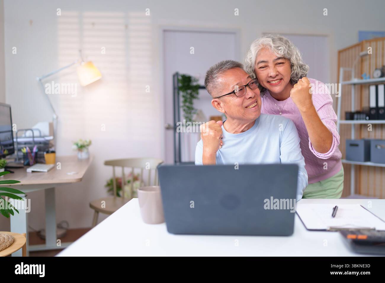 Ein älteres asiatisches Paar feiert seinen Erfolg mit einem Laptop zu Hause. Sie genießen gemeinsam ihr glückliches Ruhestand. Sie sind froh Stockfoto