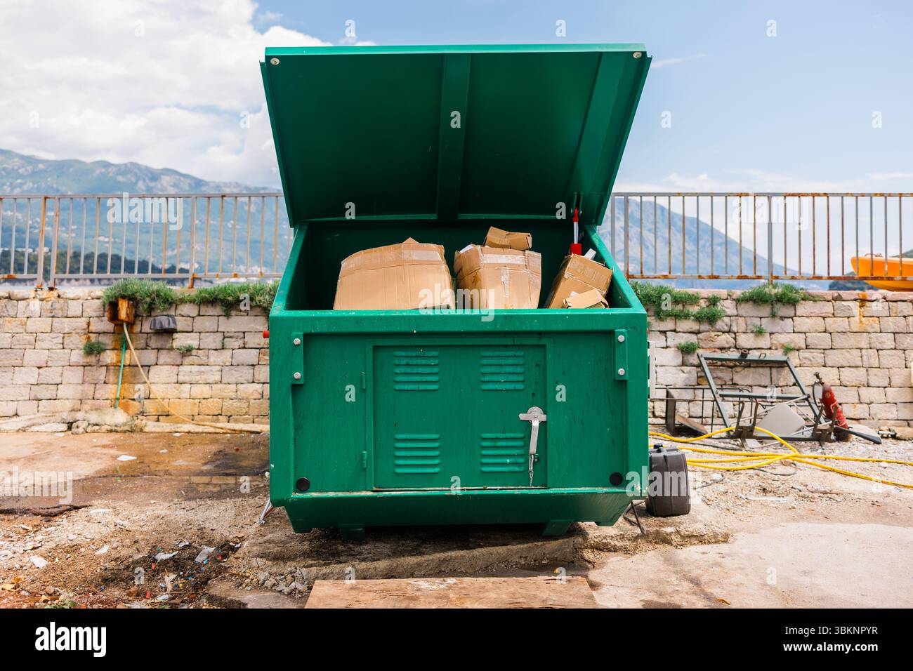 Grüner industrieller Müllcontainer gefüllt mit Kartonagen im Freien. Abfallwirtschaft, Recyclingpraktiken und Umweltverantwortung in städtischen infras Stockfoto