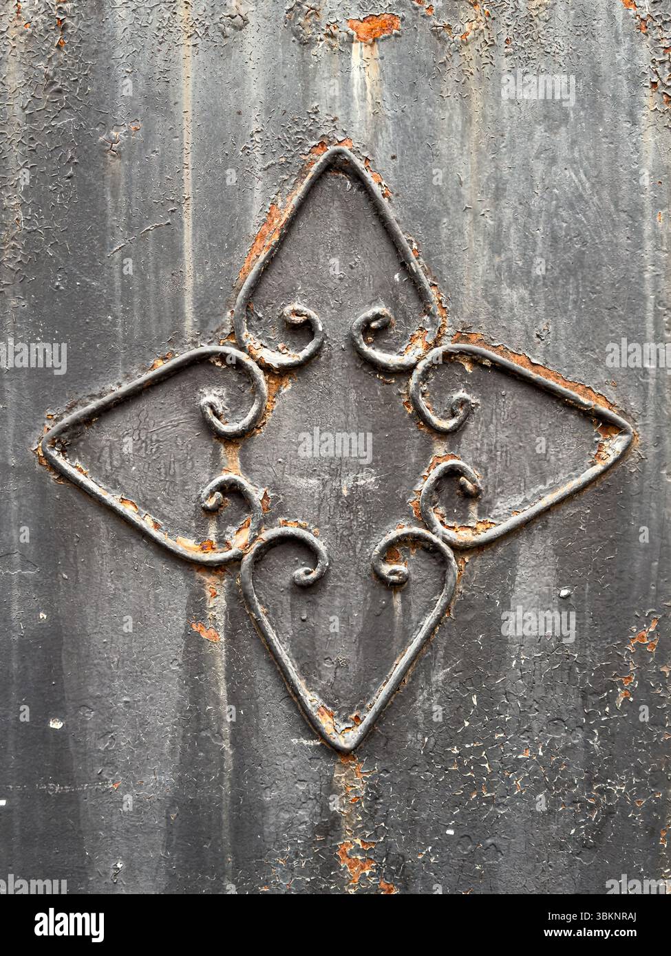 Dekorative Schmiedeeisen-Details auf strukturierter dunkler Metalloberfläche mit Rost und abblätternder Farbe. Ideal für Design, Hintergrund oder Textur. Keine Personen. Stockfoto