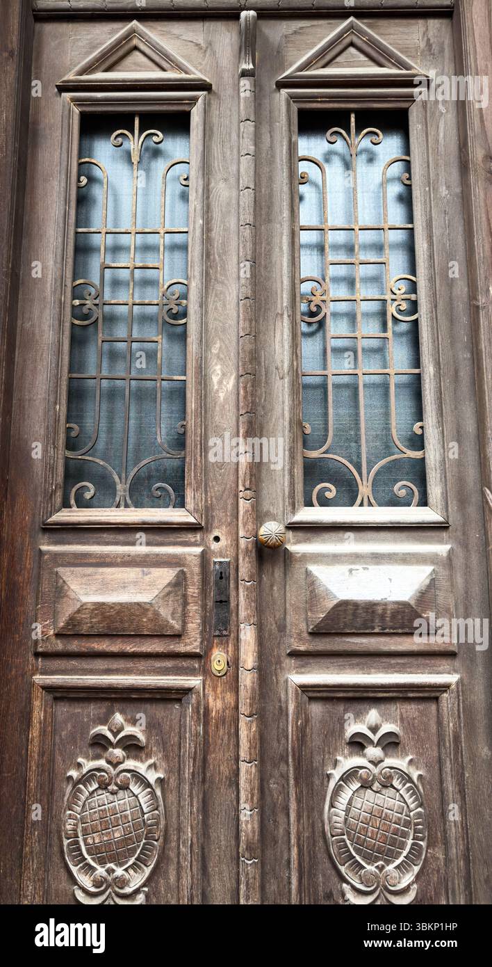 Nahaufnahme einer symmetrischen Vintage-Holztür mit geschnitzten Paneelen und dekorativen Eisengittern. Nützlich für Hintergründe oder Architekturthemen. Stockfoto