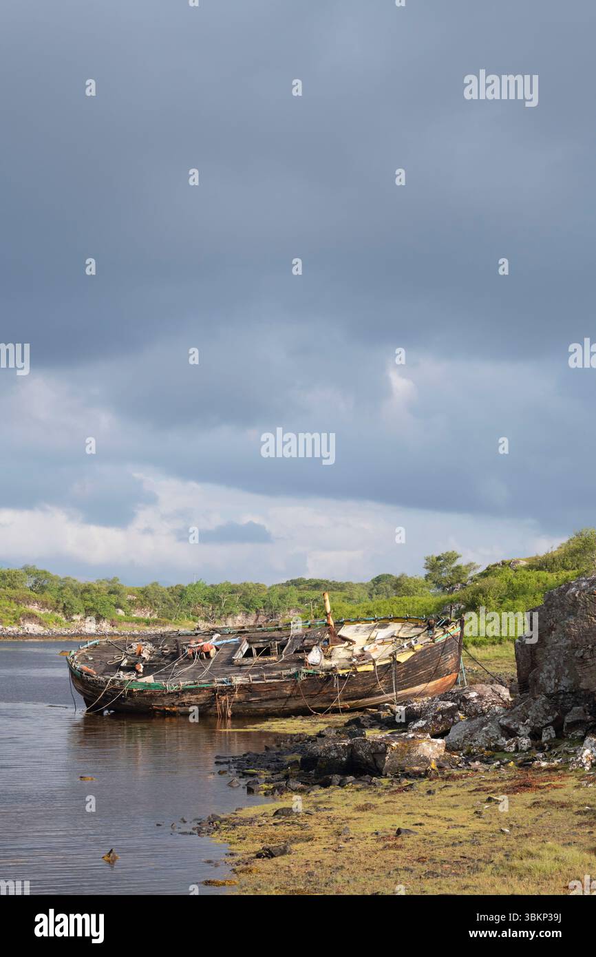 Ein verlassenes Holzfischboot an der Küste von Culduie, Applecross, das bei Ebbe am frühen Morgen bei Sonnenschein zu sehen ist Stockfoto