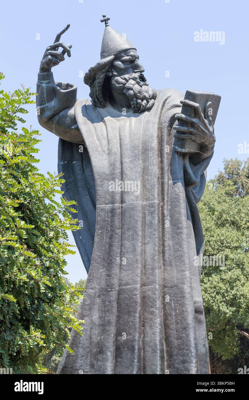 SPLIT, KROATIEN, 08.06.2018: Eine ruhige Szene mit einem historischen Glockenturm neben einer hohen Statue, umgeben von üppigem Grün, unter einem klaren blauen Himmel, Stockfoto