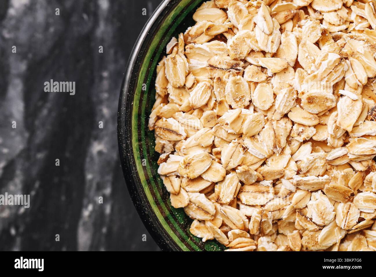 Haferflocken in dunkler Keramikschale. Gesunde Frühstückszutat auf Marmortisch. Natürliches Vollkorngetreide für vegane und Fitness-Diät. Stockfoto
